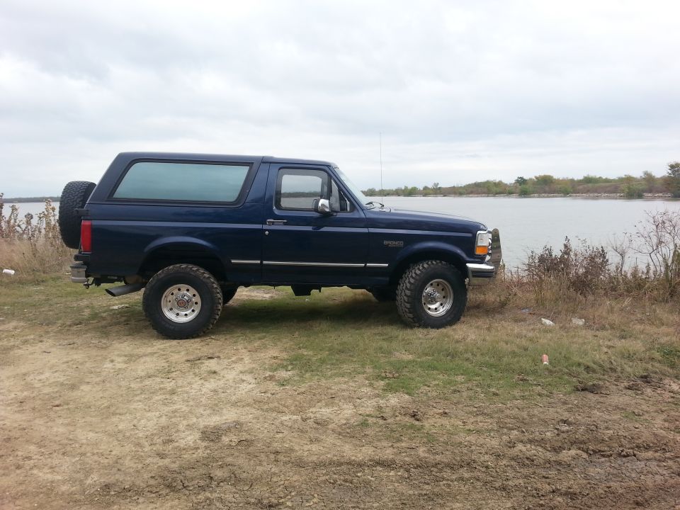 1995 Ford Bronco parked on dirt and grass next to a lake