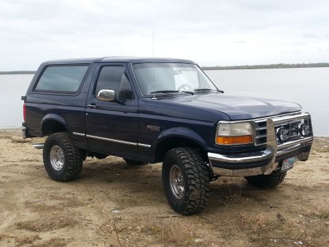 1995 Ford Bronco - 1995 Ford Bronco parked on a dirt lot with a body of water in the background.