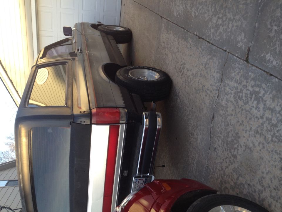 Gray 1987 Ford Bronco rear quarter view, showing a red and white stripe on the tailgate and chrome bumper
