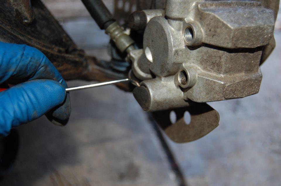 Close-up of ATV brake caliper being worked on with a tool and blue glove