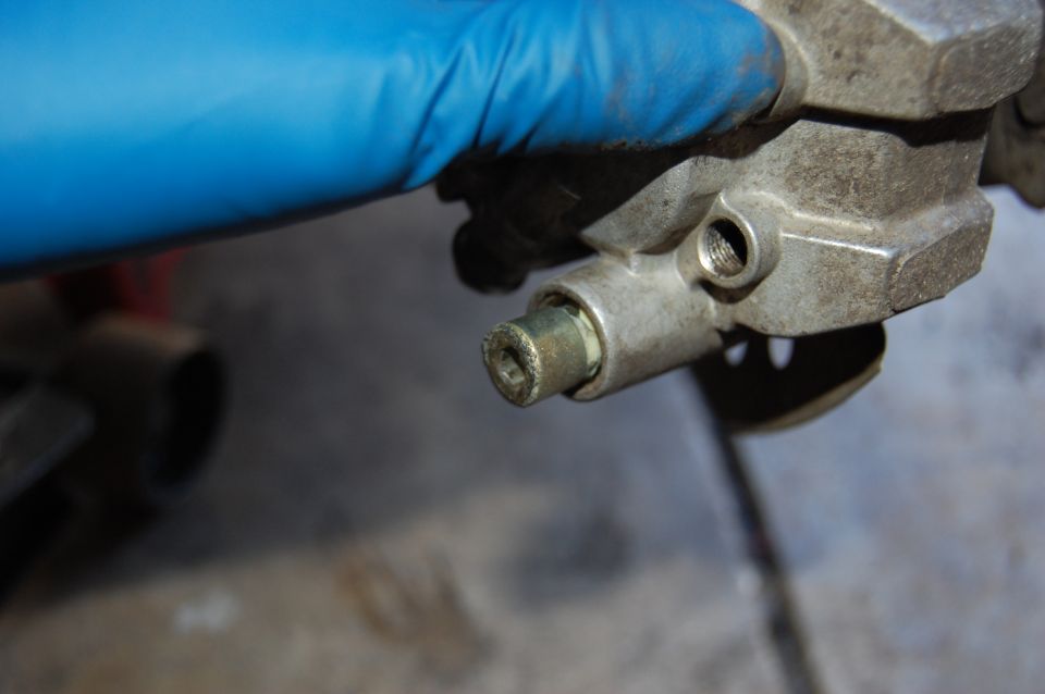 Metal part with a hex bolt, held by a blue gloved hand