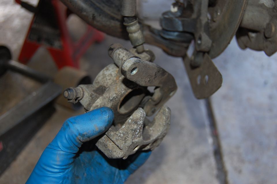Brake caliper held by a gloved hand, with a red jack stand in the background