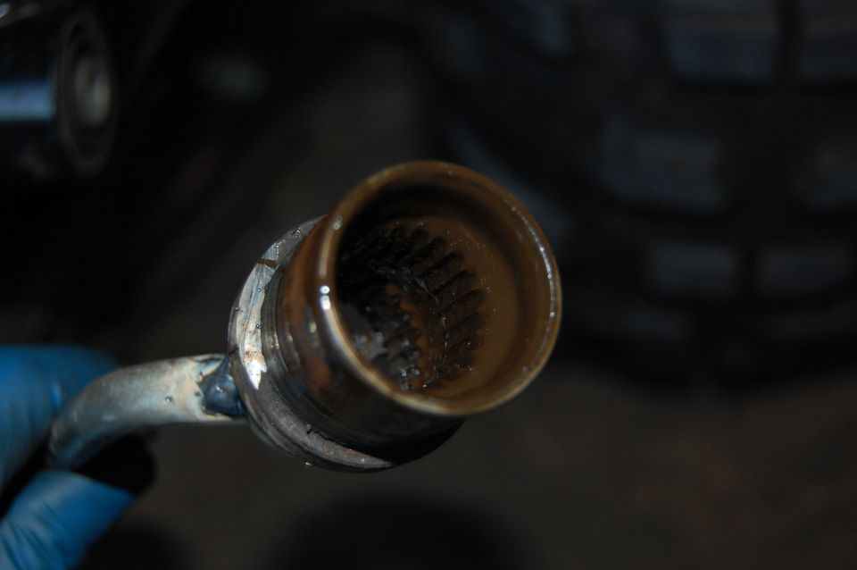 Driveshaft joint with splines, covered in grease and dirt. A blue gloved hand holds the shaft