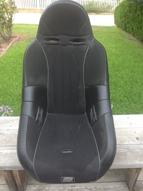 1986 Ford Bronco - Black racing seat with silver stitching and harness cutouts, placed on a wooden surface outside.