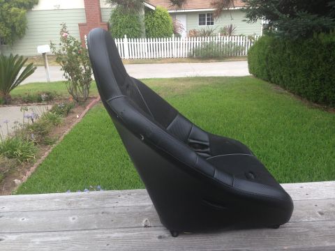 1986 Ford Bronco - A black racing seat with textured upholstery and an integrated seatbelt is shown outdoors on a wooden surface.