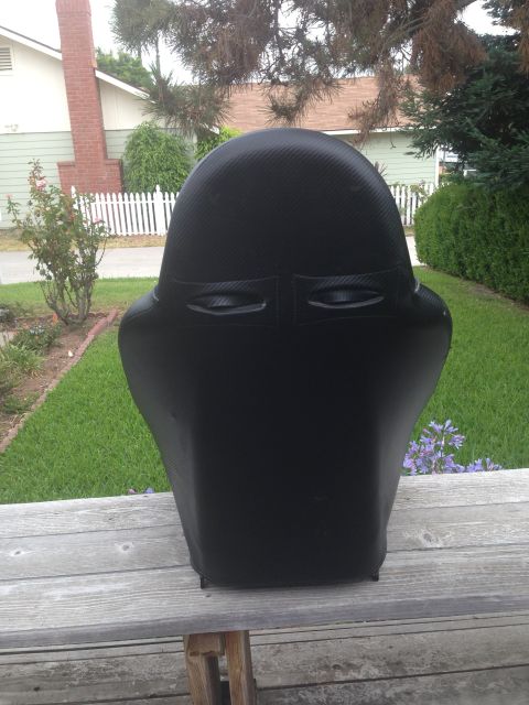 1986 Ford Bronco - A black racing seat with a carbon fiber pattern is displayed outdoors on a wooden surface.