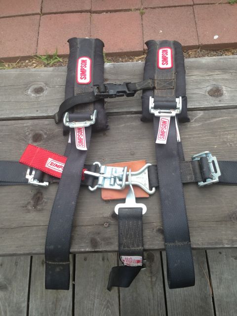 1986 Ford Bronco - Simpson racing seat belts shown on a wooden surface.