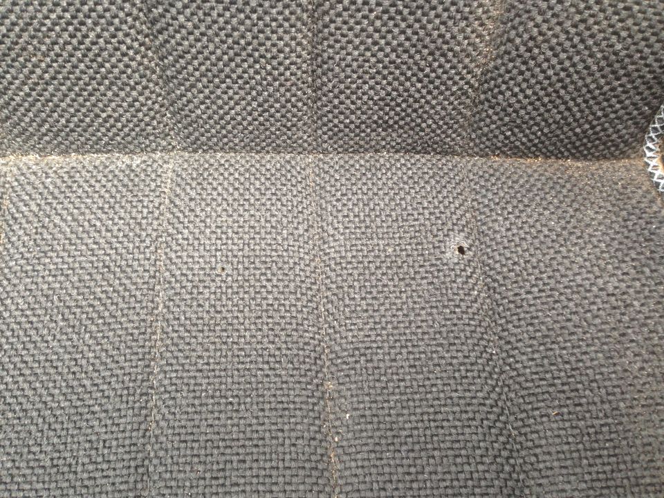 Close-up of gray woven seat fabric with a small hole