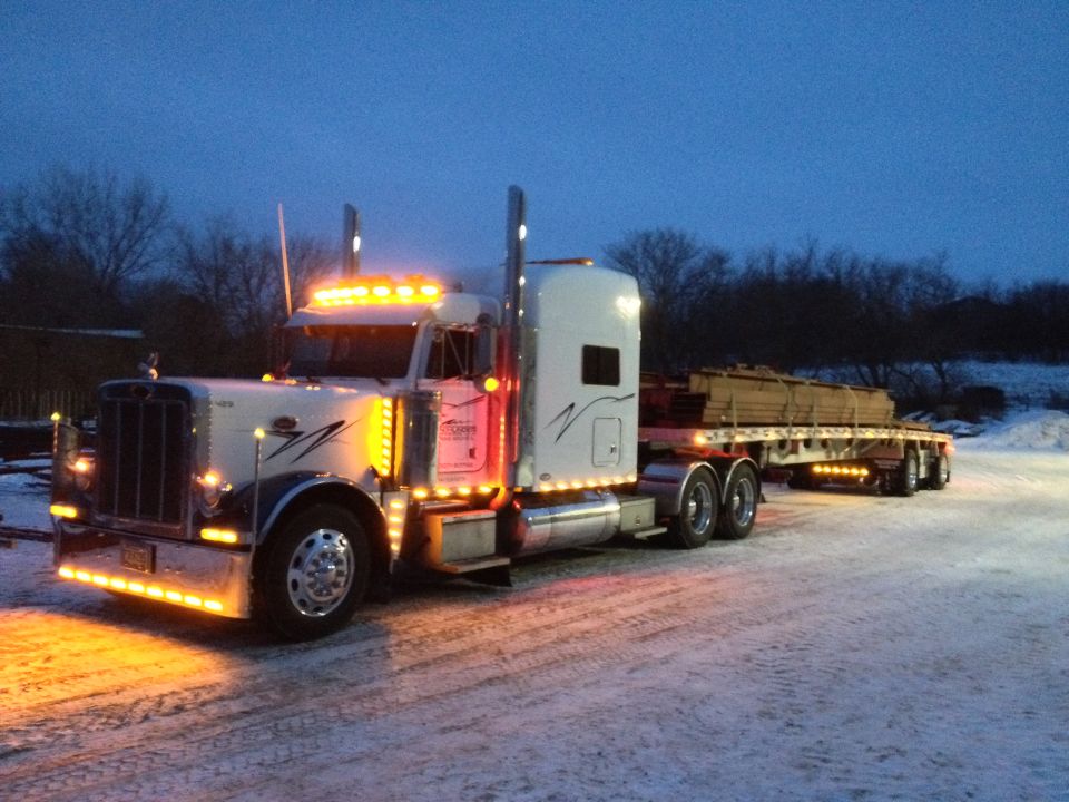 White 2003 Peterbilt 379 semi-truck with trailer loaded with lumber, parked in snow at dusk