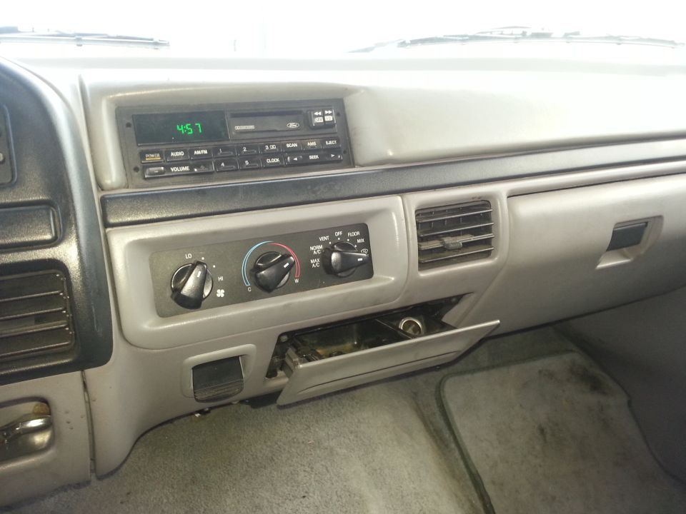 Gray dashboard interior with radio, climate controls, and open glove compartment. Clock shows 4:57