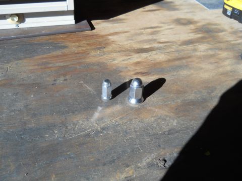 1992 Ford Bronco - Two lug nuts, one larger than the other, rest on a weathered wooden surface.