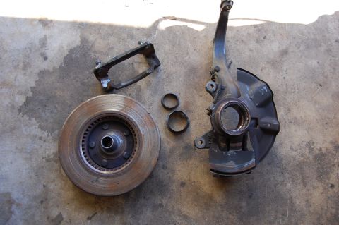 1994 Ford Bronco - Disassembled brake components including a rotor, caliper bracket, and spindle assembly are shown on a concrete surface.