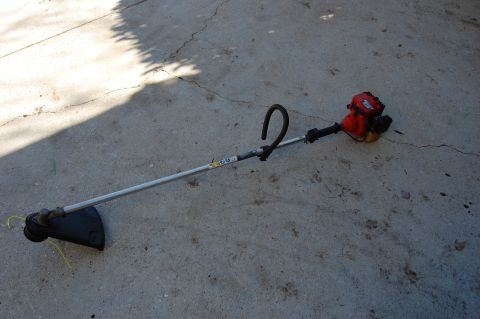 2006 Honda RANCHER - A string trimmer rests on a concrete surface, its red engine and black handle clearly visible.