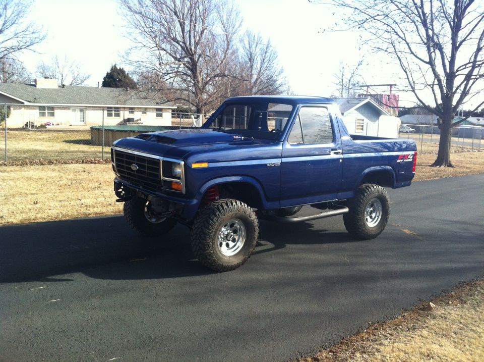 Blue lifted Ford Bronco parked on asphalt driveway in front of a house
