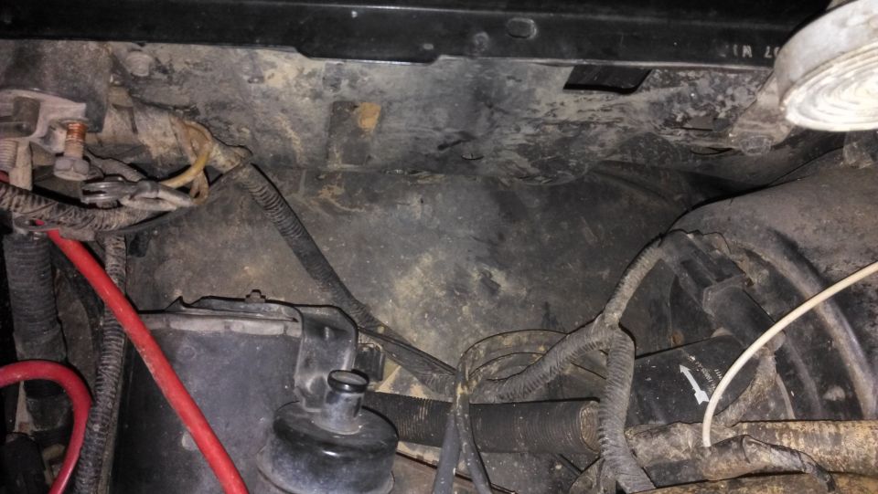 Engine bay with wiring, hoses, and battery components. Some dirt and grime are visible