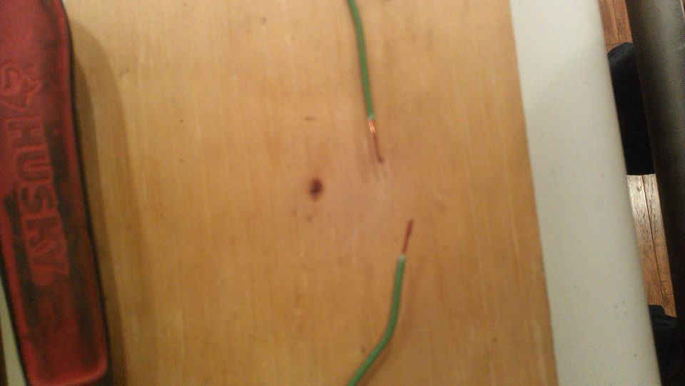 Exposed copper wire ends on a wooden surface, with a red tool handle on the left