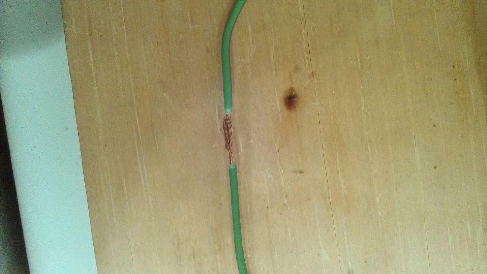 Damaged green wire with exposed copper strands on a wooden surface