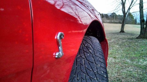 1997 Ford Mustang - A chrome cobra emblem is affixed to the side of a red vehicle, with a tire and fender well in view.
