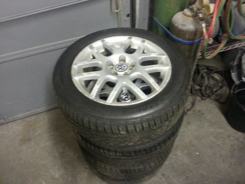 2002 Volkswagen Jetta - A set of four Volkswagen rims and tires are stacked in front of a garage door.