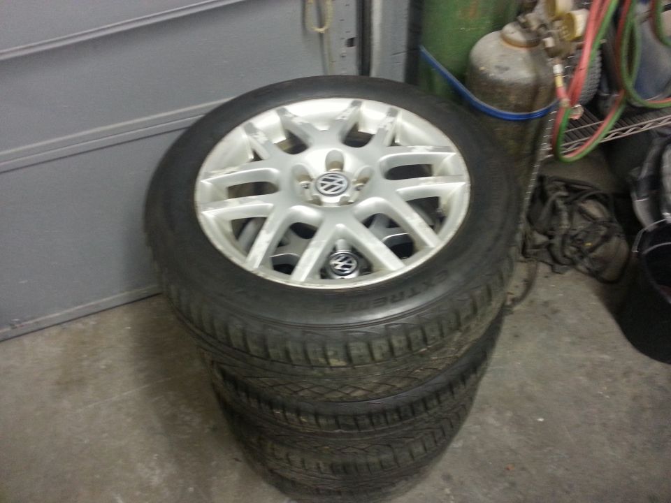Stack of four Volkswagen rims with tires. The rims have a silver finish and a multi-spoke design with the VW logo in the center