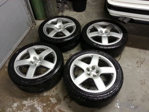 2002 Volkswagen Jetta - A set of four alloy wheels and tires are displayed in a garage setting, with a portion of a white vehicle in the background.