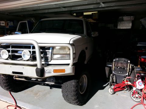 1992 Ford Bronco - A white 1992 Ford Bronco is parked in a garage, equipped with a bull bar and large tires.