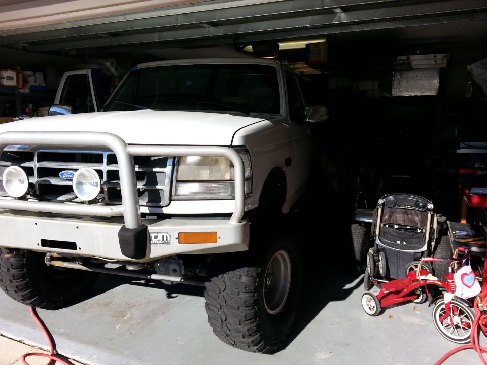 White Ford Bronco with a bull bar and off-road tires parked in a garage