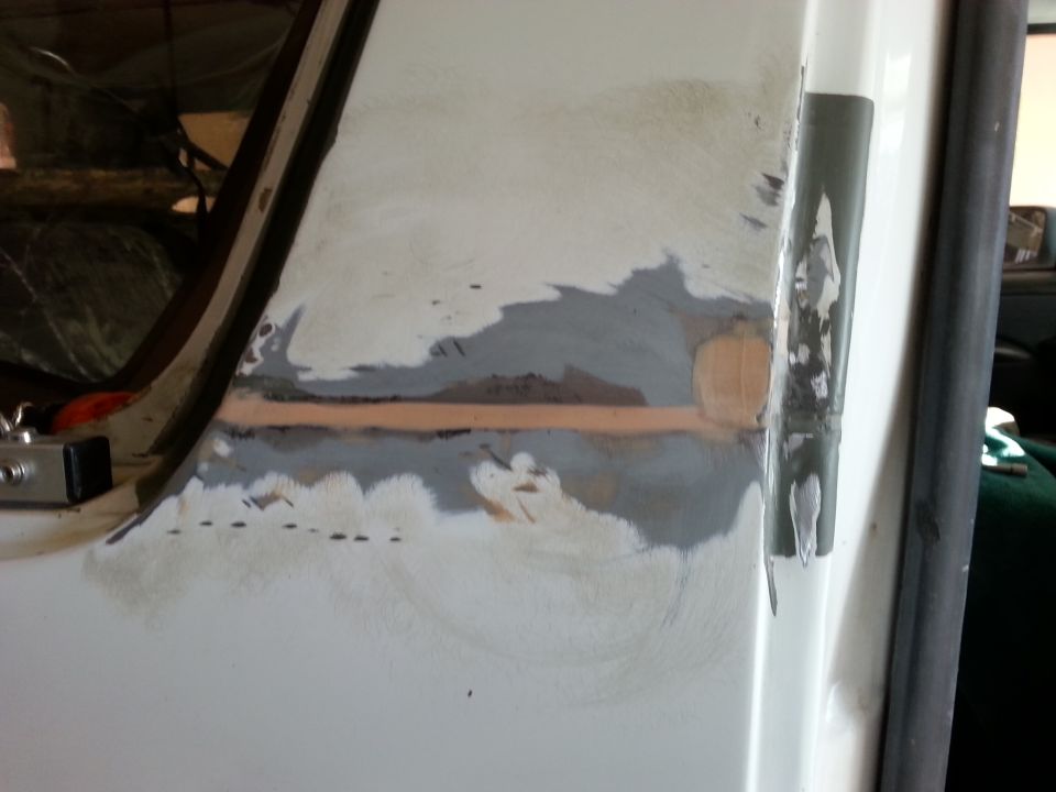 Close-up of body filler and primer on a vehicle's door frame, showing repair work