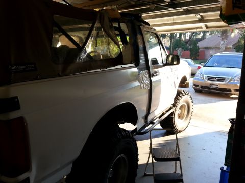 1992 Ford Bronco - A white Ford Bronco with a soft top and off-road tires is parked in a garage, with another vehicle in the background.