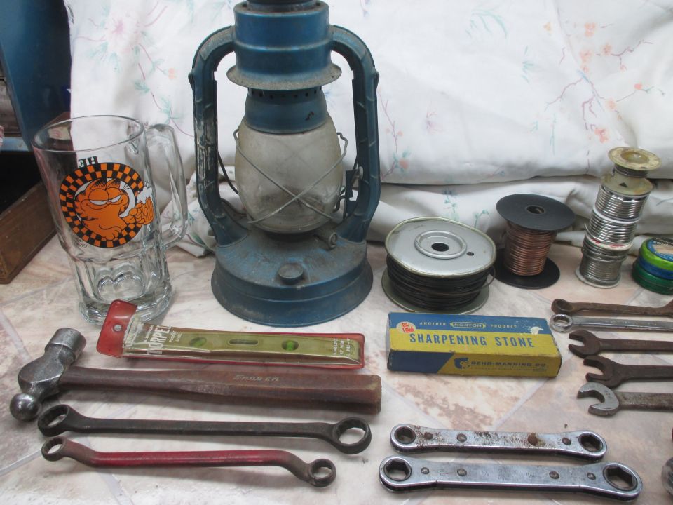 Collection of tools including wrenches, a hammer, a level, and a sharpening stone box, next to a blue lantern and a Garfield mug