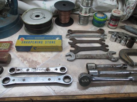 2004 Aston Martin Virage - A variety of tools and hardware are laid out on a tiled surface, including wrenches, a sharpening stone, and spools of wire.