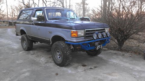 1990 Ford Bronco - This Ford Bronco has a custom blue front bumper with winch and auxiliary lights, suggesting off-road modifications.