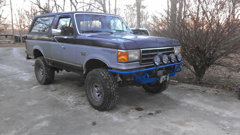 Blue and gray Ford Bronco with aftermarket blue front bumper and four auxiliary lights