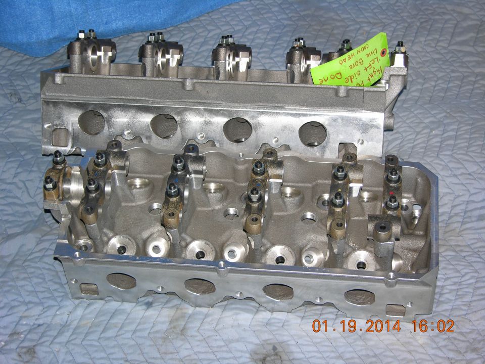 Two engine cylinder heads, one stacked on top of the other. A green sticky note is attached to the top head