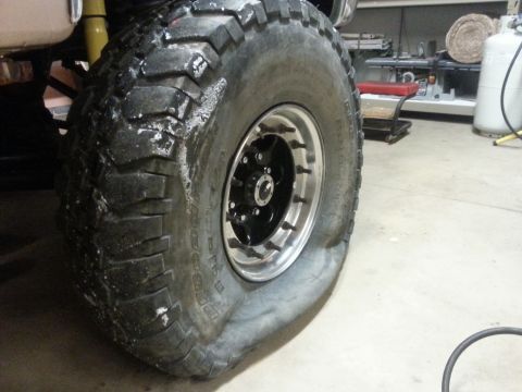 1996 Ford Bronco - A flat tire on a lifted truck with aftermarket wheels is shown in a garage.