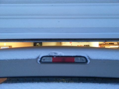 1996 Ford Bronco - A snow-covered rear brake light on a vehicle is visible through a gap in a garage door.