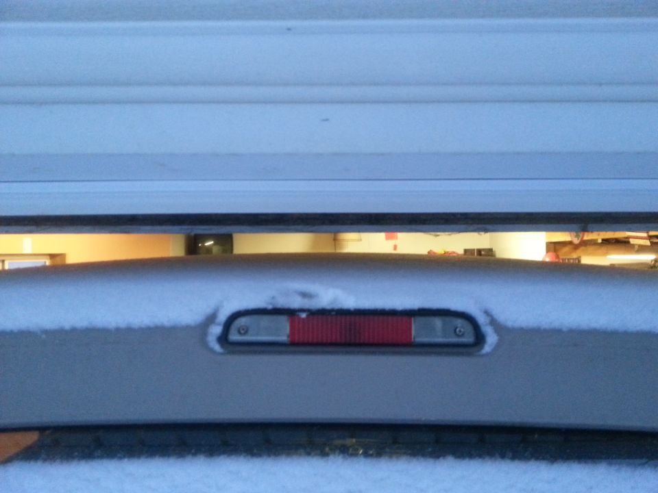 Silver SUV rear brake light covered in snow, partially obscured by a garage door