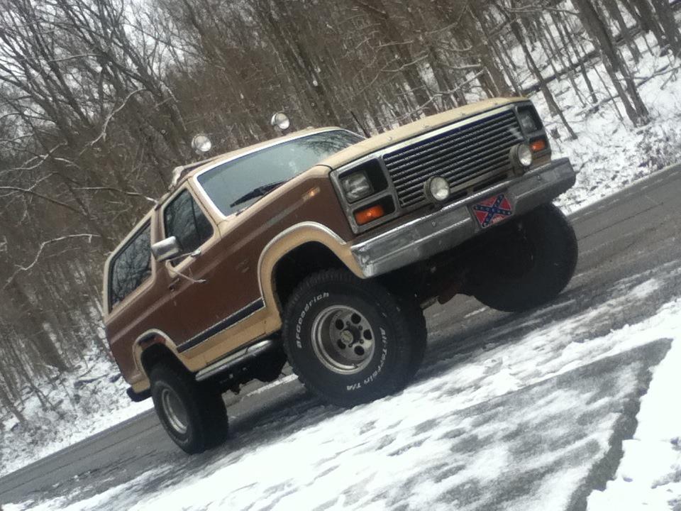 Brown and tan SUV with off-road tires and auxiliary lights on the roof. Rebel flag plate