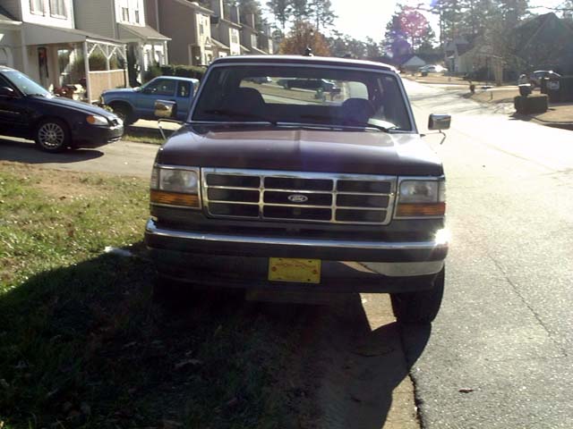 Front view of dark maroon Ford Bronco with chrome grille parked on grass beside a residential street