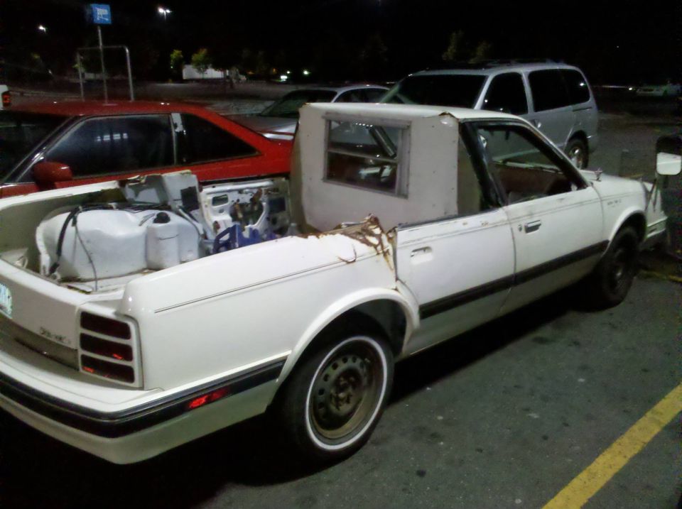 White coupe utility, rear quarter view, exposed engine and fuel tanks in bed, damaged canopy