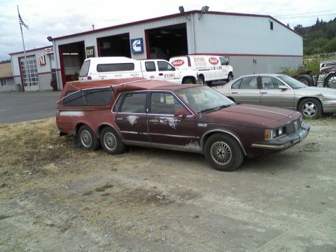 1972 Ford Ranchero - This custom six-wheeled station wagon has a camper shell extension and is parked in front of a commercial building.