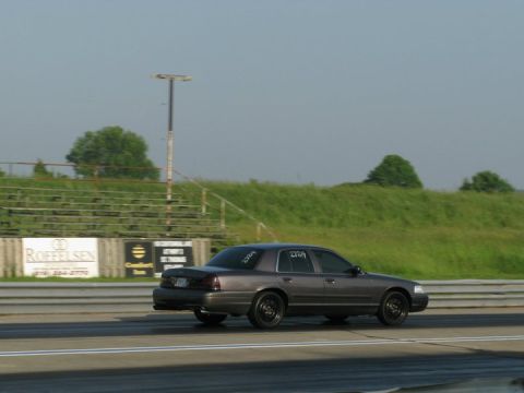 2004 Ford Crown Victoria - A gray 2004 Ford Crown Victoria is seen on a drag strip with racing numbers on its window.