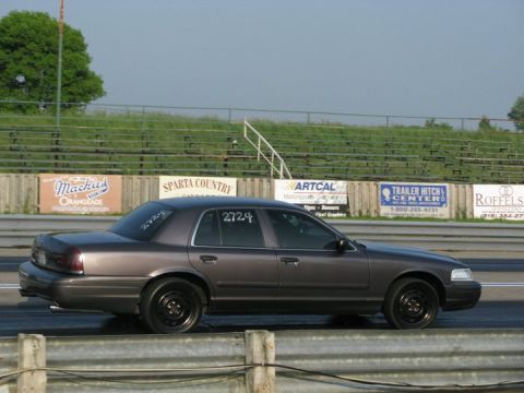 2004 Ford Crown Victoria - A gray Ford Crown Victoria is parked on a drag strip, with racing numbers visible on its windows.