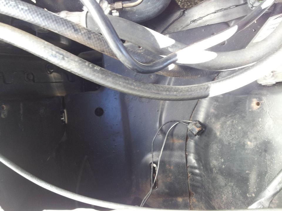Engine bay with hoses and wiring, dark metal surfaces, some rust spots