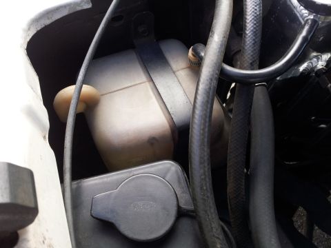 1976 Ford Ranchero - Close-up view of a vehicle's engine bay, focusing on the radiator overflow tank and associated hoses.