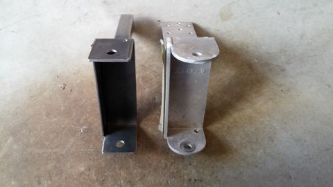 1985 Toyota 4Runner - Comparison of two awning brackets, one made of dark metal and the other of silver metal, displayed on a concrete surface.