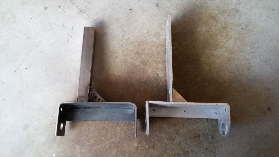 Two custom metal brackets, one with triangular bracing, sit on a concrete floor