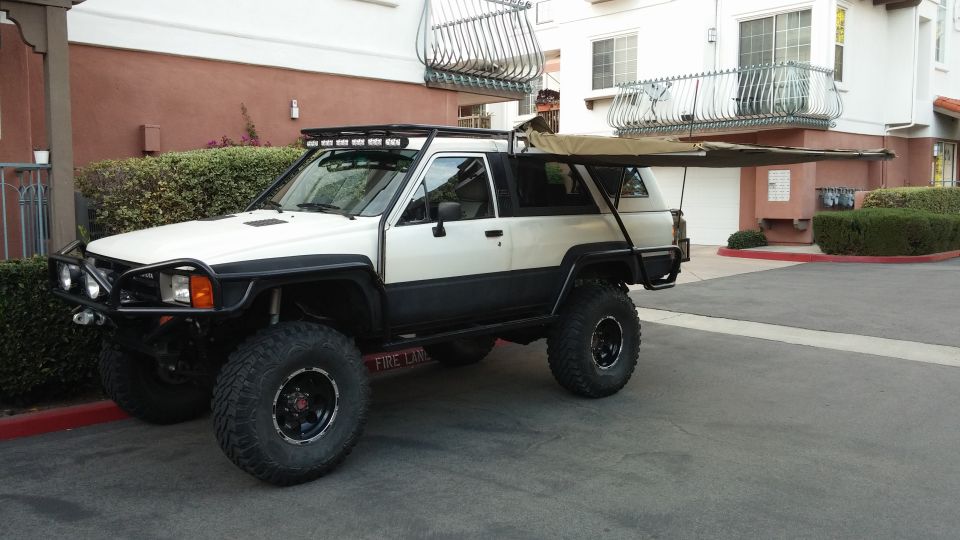 White and black Toyota 4Runner with off-road tires, roof rack, and extended awning