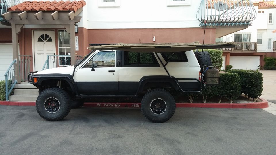 White and black SUV with awning, large tires, and spare tire carrier