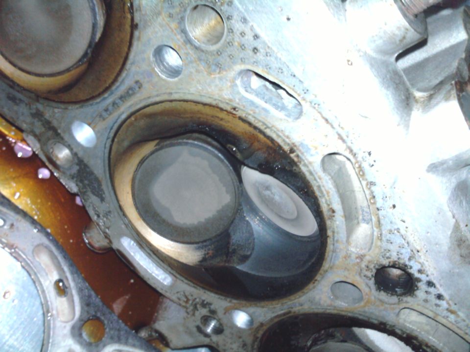 Close-up of an engine cylinder head showing two valves and combustion chambers. Some oil residue is visible